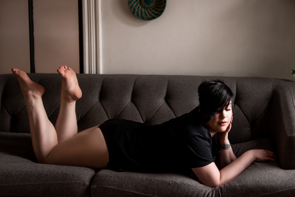 A mature curvy woman in a black t-shirt lying on a couch on her stomach.